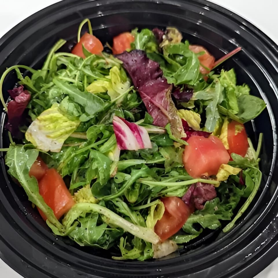 A fresh Italian salad with mixed greens, arugula, and diced tomatoes in a black bowl.