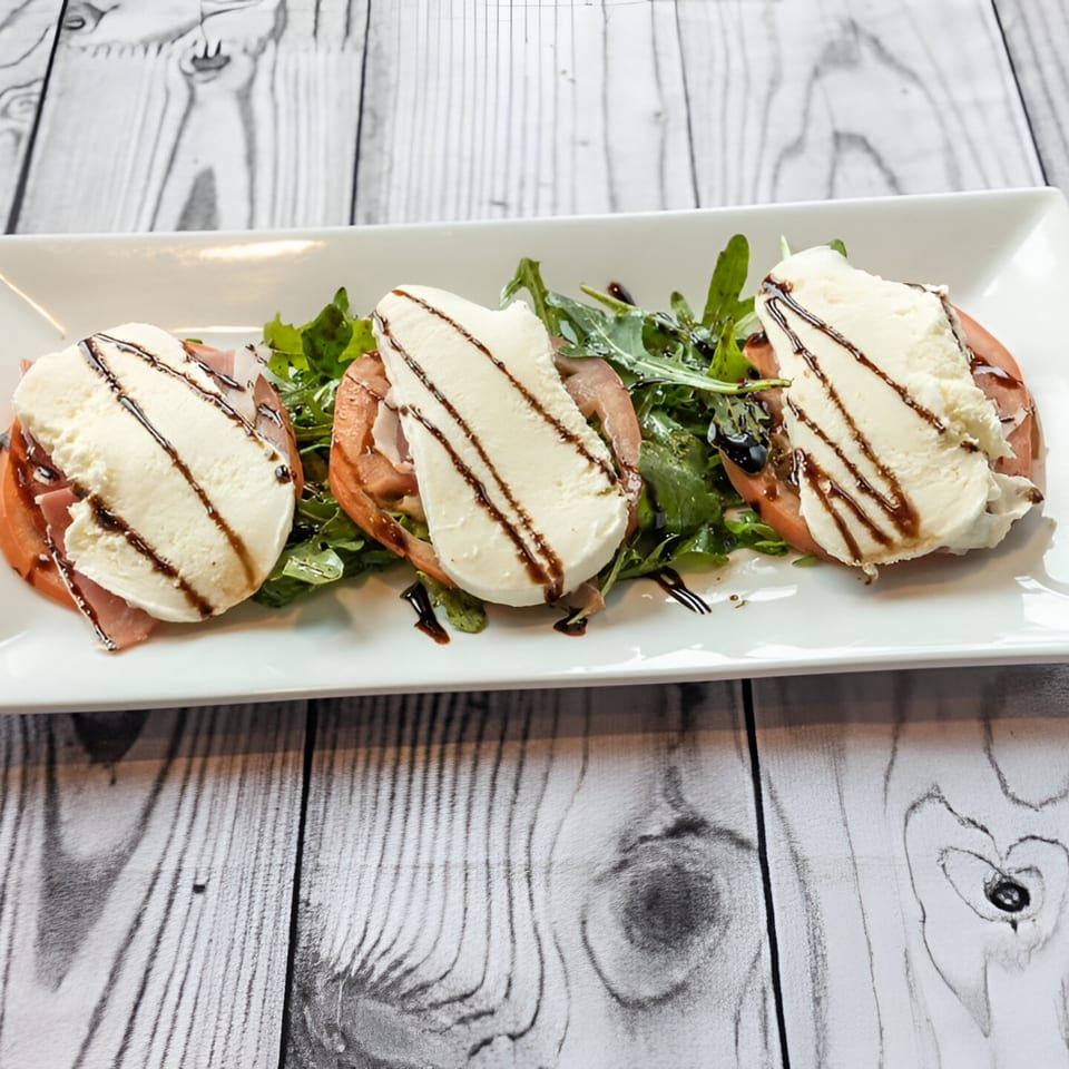 Three servings of Pavesi Restaurant's Italian Caprese salad with balsamic glaze on a white plate.