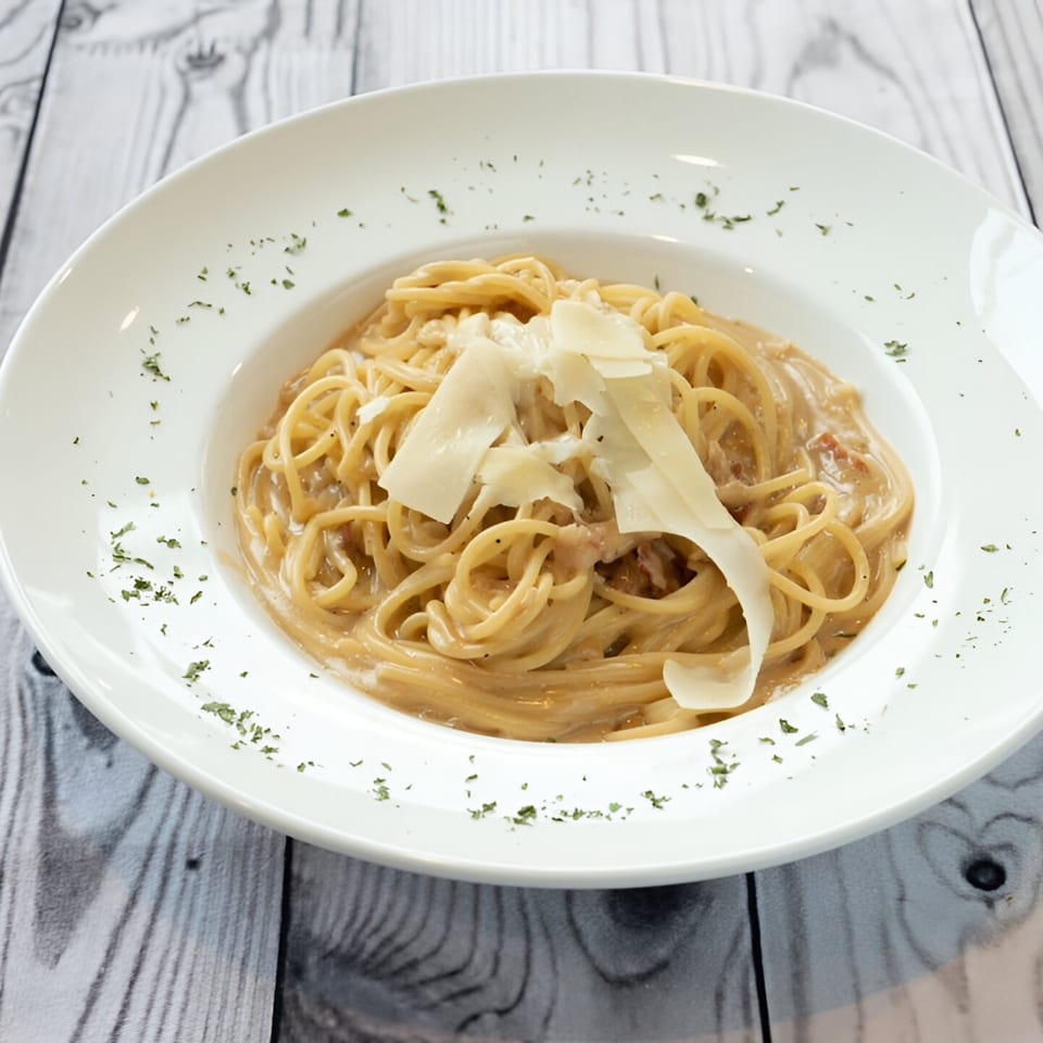 Pavesi Restaurant's spaghetti carbonara, topped with shaved parmesan and parsley, on a white plate.