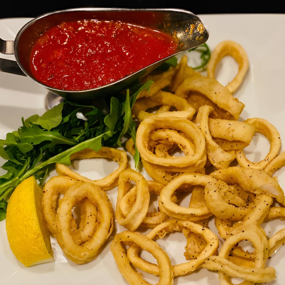Crispy fried calamari rings with a side of marinara sauce, arugula, and a lemon wedge.