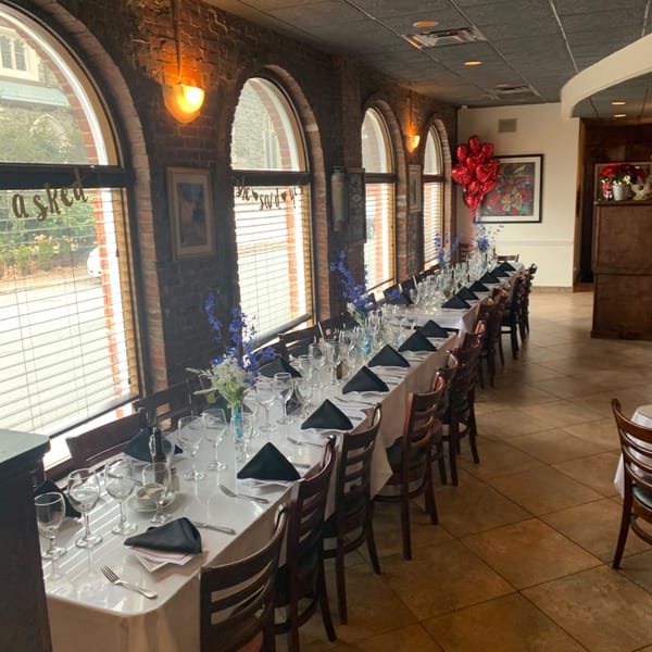 Long dining table set for a private event at Pavesi Restaurant, with arched windows and brick walls.