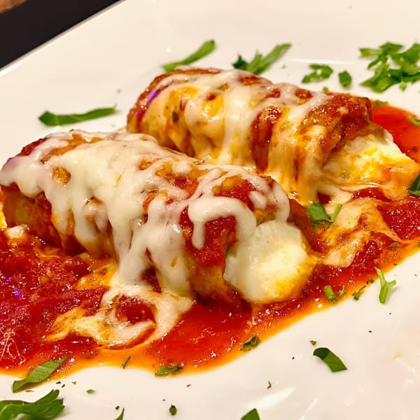 Two baked Italian manicotti covered in melted cheese, marinara sauce, and parsley on a white plate.