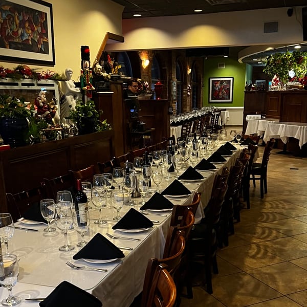 Long dining table set with white tablecloths, black napkins, wine glasses, and bottles in Pavesi Restaurant.