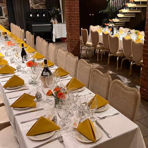 Long tables set with white tablecloths, yellow napkins, wine bottles, and floral centerpieces at Pavesi Restaurant.