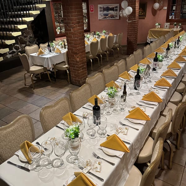 Long dining tables set with white tablecloths, gold napkins, wine bottles, and glasses in Pavesi Restaurant.