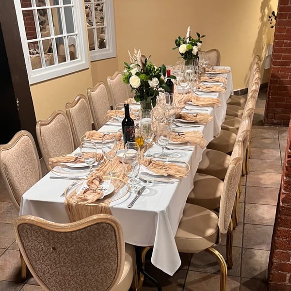 Long dining table set for a Pavesi Restaurant event with white tablecloths, gold runners, and floral centerpieces.